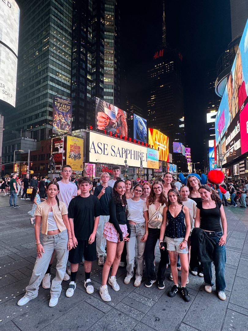 Groupe d’ados CEI devant les écrans lumineux de Times Square à New York la nuit