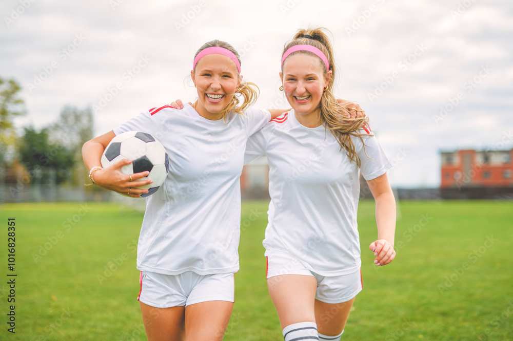 Deux jeunes joueuses de football en tenue blanche sourient et courent ensemble sur un terrain de football, illustrant l’ambiance conviviale et dynamique du séjour football en Irlande.