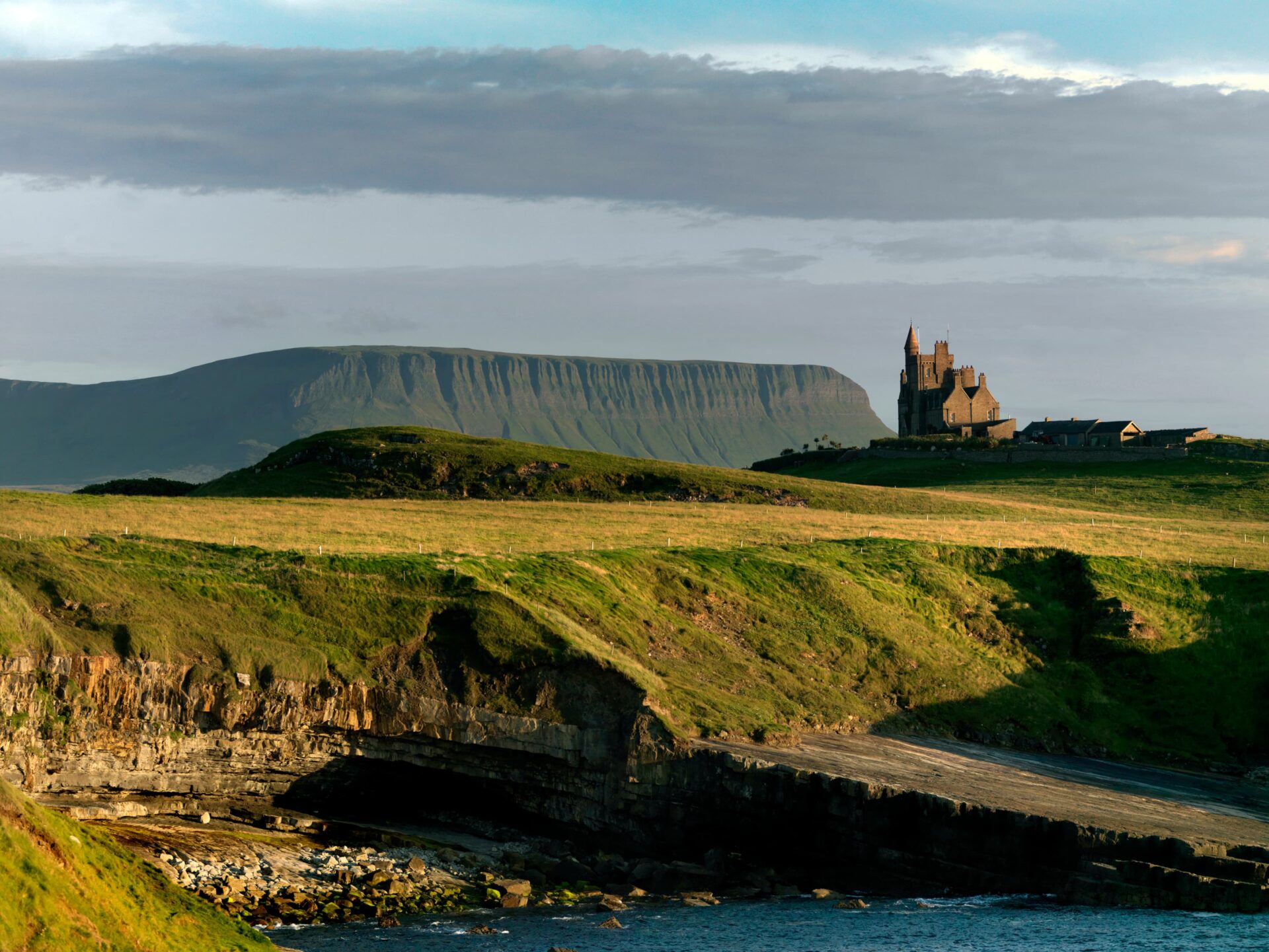 Paysage verdoyant du comté de Sligo, avec une falaise, un château sur une colline et une montagne en arrière-plan, illustrant la beauté naturelle et le charme de l’Irlande.