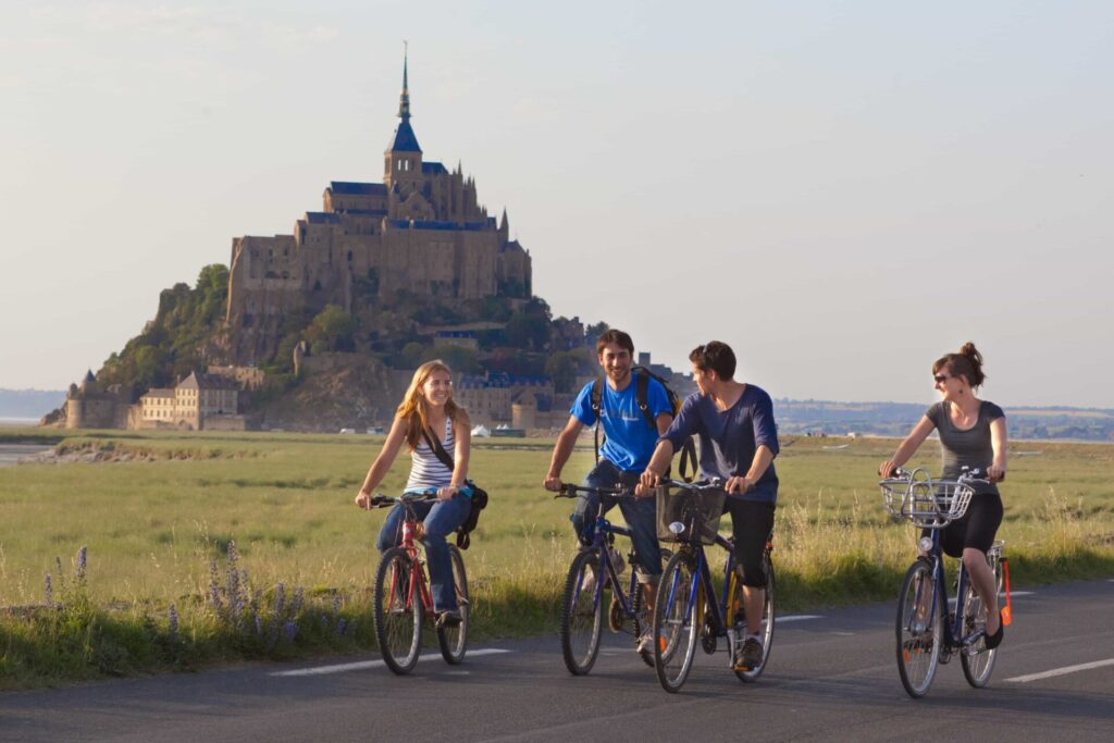 Students on a CEI stay in France biking with Mont Saint-Michel in the background and enjoying cultural discovery in the great outdoors.