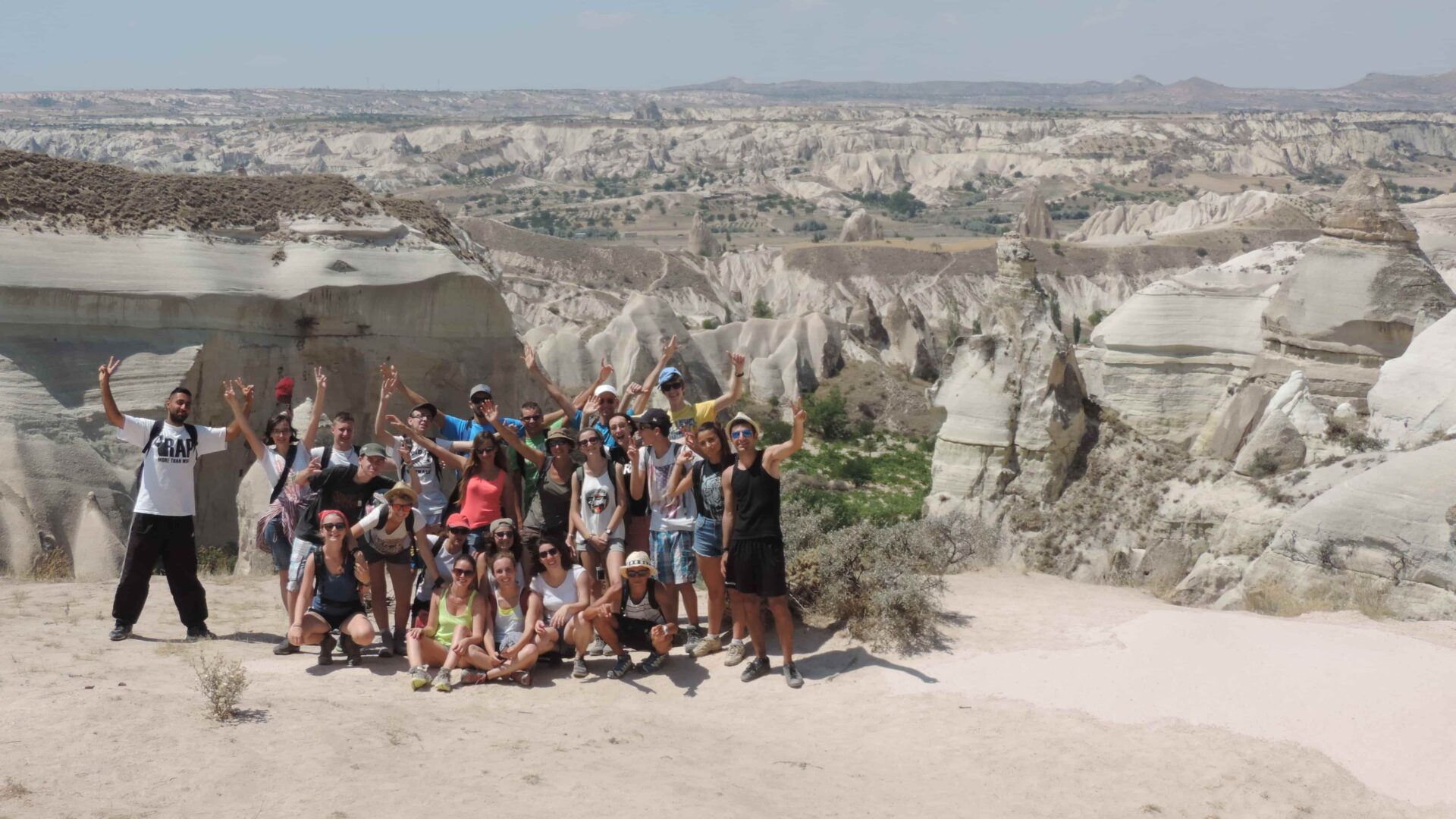 Groupe de jeunes en randonnée pendant une colonie de vacances en Cappadoce, bras levés au milieu des formations rocheuses.