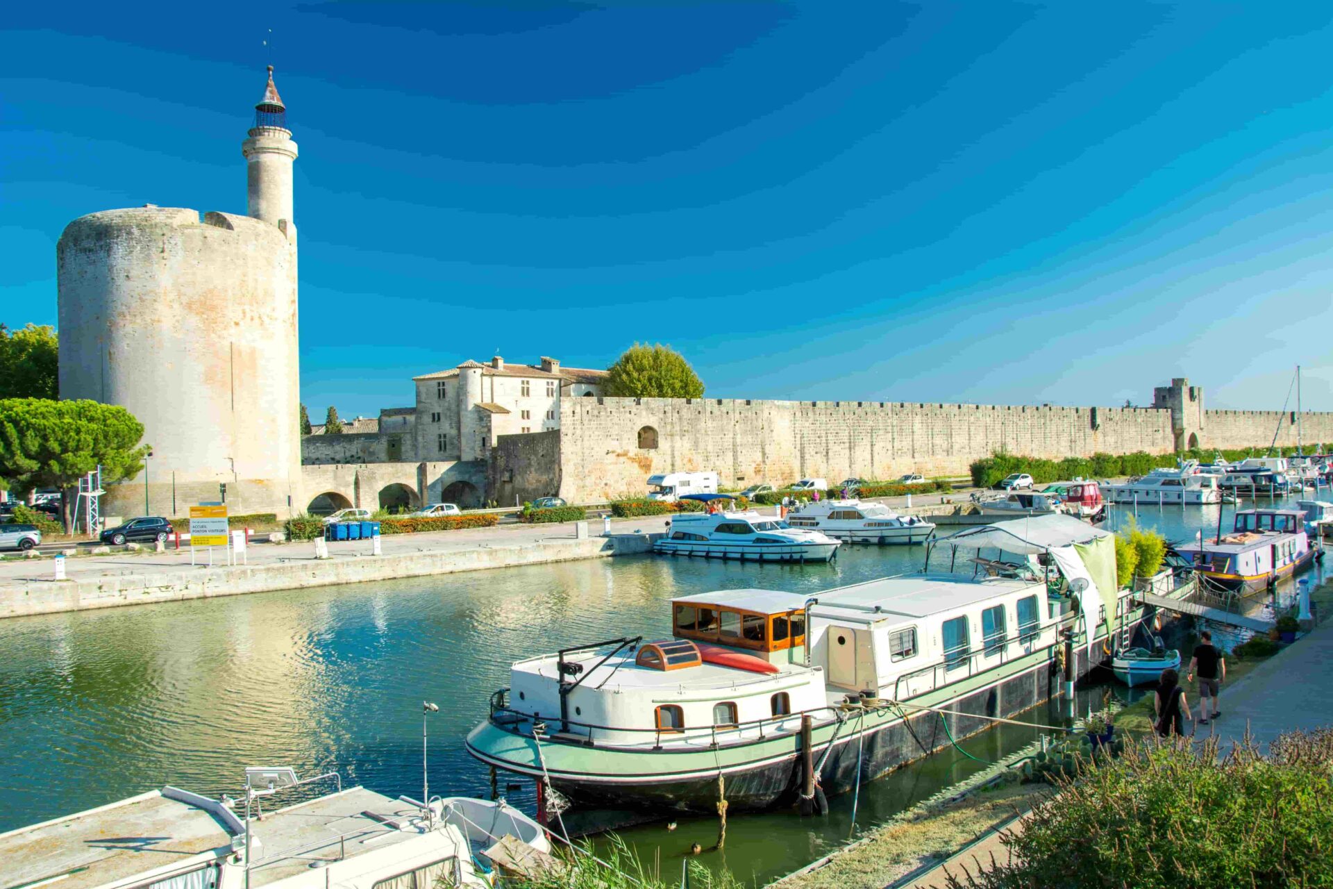View of the medieval walls and canal boats in Aigues-Mortes under a clear blue sky, part of the CEI international camp excursion.