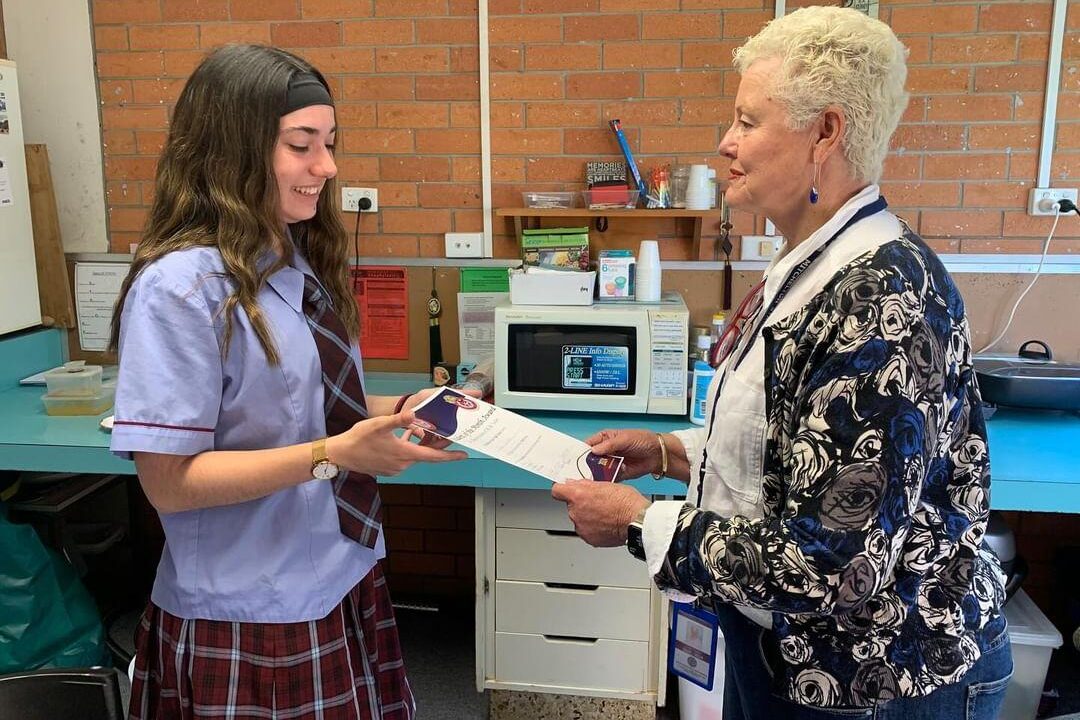 Élève en uniforme australien recevant un document de son enseignante dans un lycée.